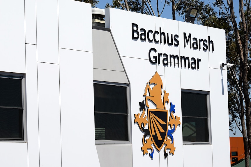 A logo of a school on a white building with trees in the back.