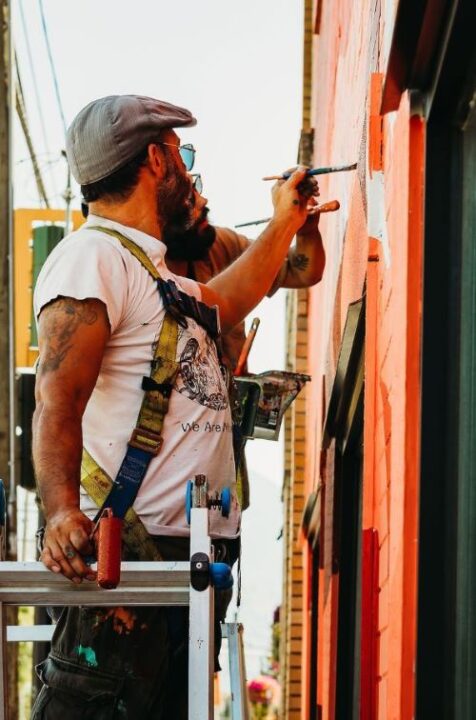 Man dressed in white tshirt, holding a paintbrush, painting a mural