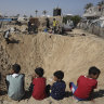 Palestinian children sit at the edge of a crater after an Israeli airstrike in Khan Younis.