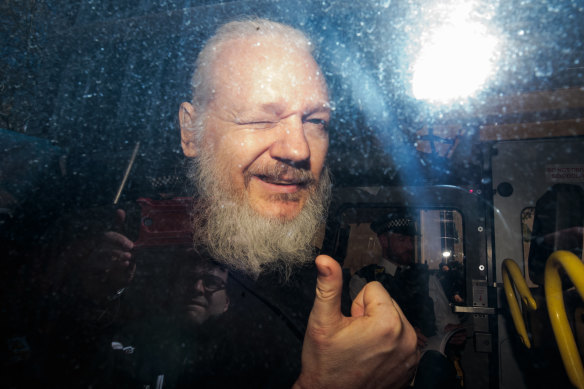 Julian Assange gestures to the media from a police vehicle on his arrival at Westminster Magistrates court in London, England.