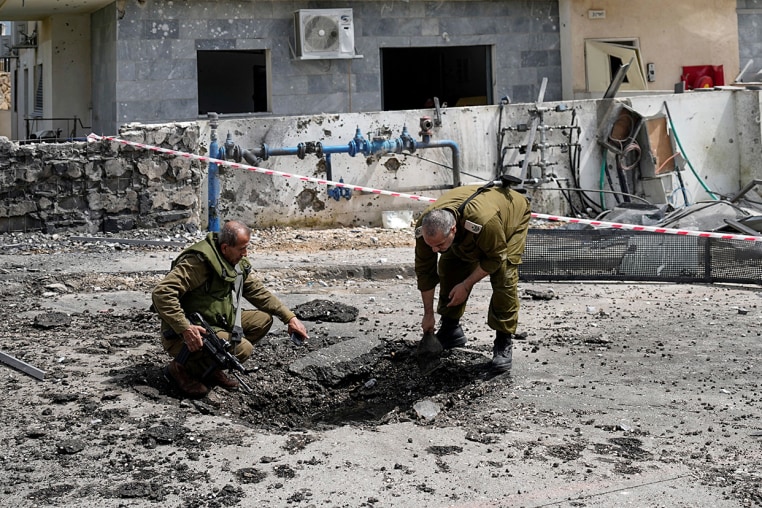 Two Israeli security forces look at damage created by rocket fired from Lebabon