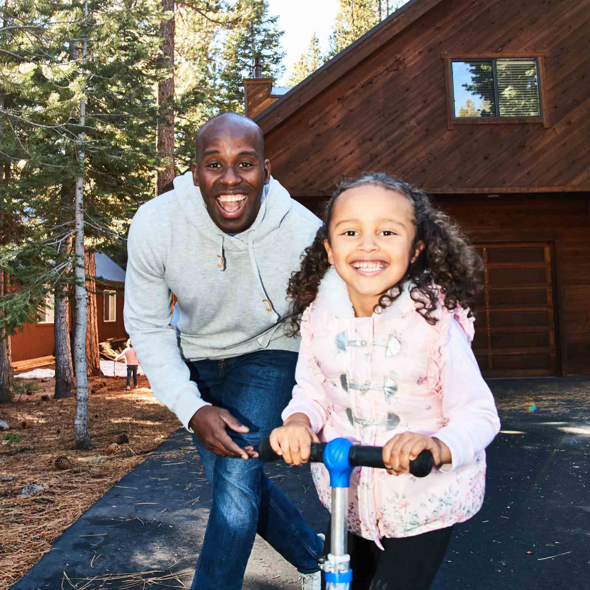 A smiling father-daughter duo play outside of a log cabin.