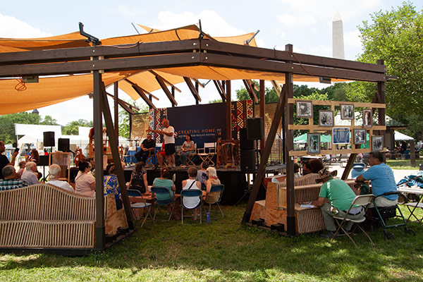 People speaking on an outdoor stage for an audience.