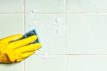 A human hand cleaning washing tiled surface in bathroom or kitchen