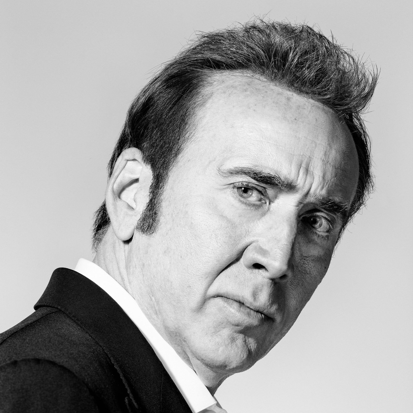 A blackandwhite portrait of Nicolas Cage who is wearing a suit and looking at the camera.