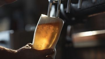 Fresh beer filling the glass directly from the tap.  With extra foam spilling over glass.