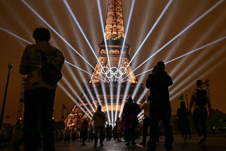 Attendees take pictures of the Eiffel Tower as lasers light up the sky during the opening ceremony of the Paris 2024 Olympic Games in Paris on July 26, 2024.