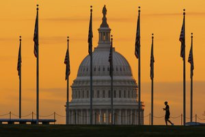 An early morning pedestrian is silhouetted against sunrise as he walks through the U.S. Flags on the National Mall and past the US Capitol Building in Washington Monday, Nov. 7, 2022, one day before the midterm election will determine the control of the US Congress.