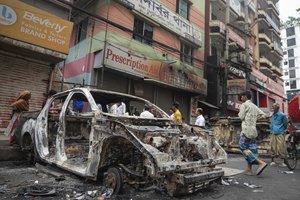 People walk past a vandalised car in Dhaka, Bangladesh, Tuesday, Aug. 6, 2024.