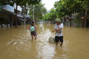 Local resident Chu Van Hai pulls a bottle of drinking water and his wife Nguyen Thi Hoa carries food in a flooded street in the aftermath of Typhoon Yagi, in Hanoi, Vietnam on Thursday, Sept. 12, 2024.