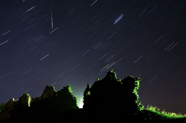 A long exposure picture of a Perseid meteor crossing the night sky and stars trails.