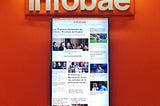 A computer monitor displays the homepage of infobae.com, an Argentine news website. The wall behind it is bright orange.