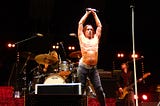 Iggy Pop onstage, holding a microphone overhead.