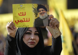 In this April 13, 2018, file photo, a supporter of Hezbollah leader Sayyed Hassan Nasrallah holds up his portrait with Arabic words that read: "We belong with you," during an election campaign speech in a southern suburb of Beirut, Lebanon