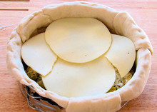 Thin, round slices of Provolone cheese arranged on top of a stuffed pizza in a springform pan, ready to bake