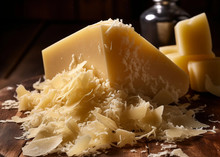 A large piece of Parmesan cheese, accompanied by small chunks and flakes, arranged on a wooden surface