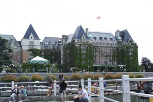 Tourists sit at the wooden benches at the Inner Harbour in Victoria, British Columbia, Canada as the famous Fairmont Empress or The Empress  lies on the background.