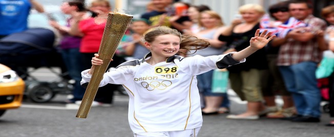 Young Torchbearer, Emma Gibbs, waves at the crowd whilst running with the Olympic Flame during the London 2012 Olympic Torch Relay.