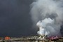 Fire fighters in protective gear watch as smoke continues to billow out after an explosion at a warehouse in northeastern China's Tianjin municipality, Thursday, Aug. 13, 2015.  