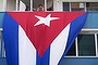 A man stands at his balcony above a Cuban flag, next to the U.S embassy building (not pictured), in Havana, Cuba August 11, 2015. U.S. Secretary of State John Kerry will travel to Cuba on August 14 to formally re-designate the U.S. Interests Section as the U.S. Embassy in Havana.