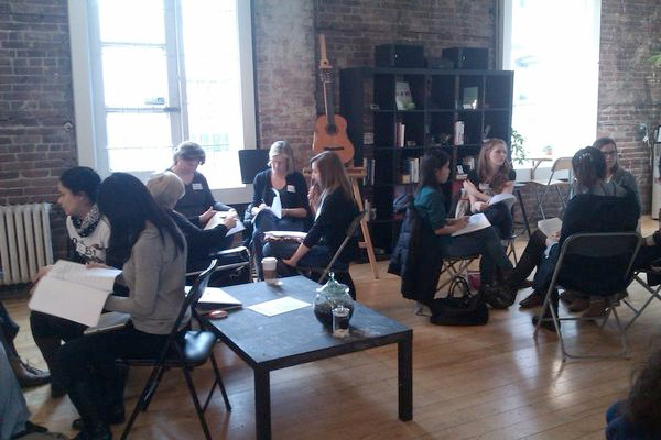 Small groups of women sitting in circles, talking and holding paper