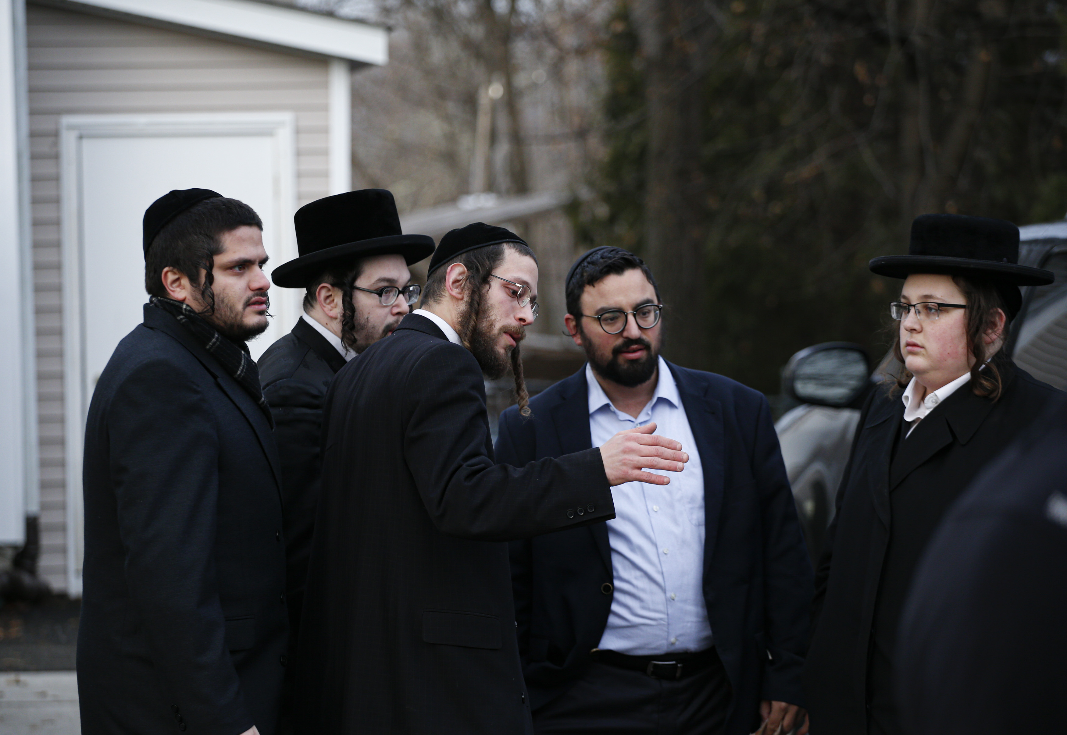 Men in Orthodox Jewish attire stand outside a house and talk to one another.