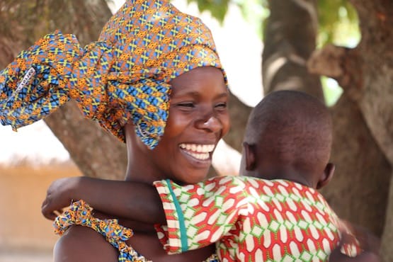 Smiling woman in patterned head wrap hugging baby