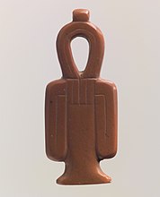 A red stone amulet shaped like a column with a looped top and two loops hanging at the sides