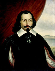 A half-length portrait of a man, set against a background that is a red curtain to the left and a landscape scene to the right. The man has medium-length dark hair, with a goatee and a wide mustache that is crooked up at the ends. He is wearing a white shirt with a wide collar, covered by a darker surcoat. There is also a bright red cape.