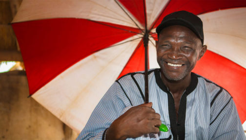 Volunteer community distributor Mamadou Samine from Senegal smiles broadly while holding an umbrella.