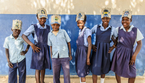 A group of students in blue uniforms, wearing paper masks on their heads.