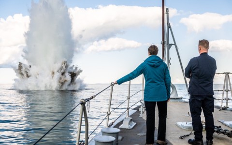 President Kersti Kaljulaid on board the Admiral Cowan, looking on at the plume of water thrown up by the destruction of a World War Two-era German sea mine.