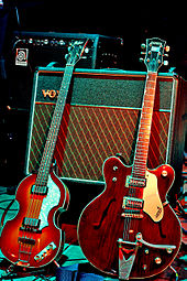 Two electric guitars, a light brown violin-shaped bass and a darker brown guitar resting against a Vox amplifier