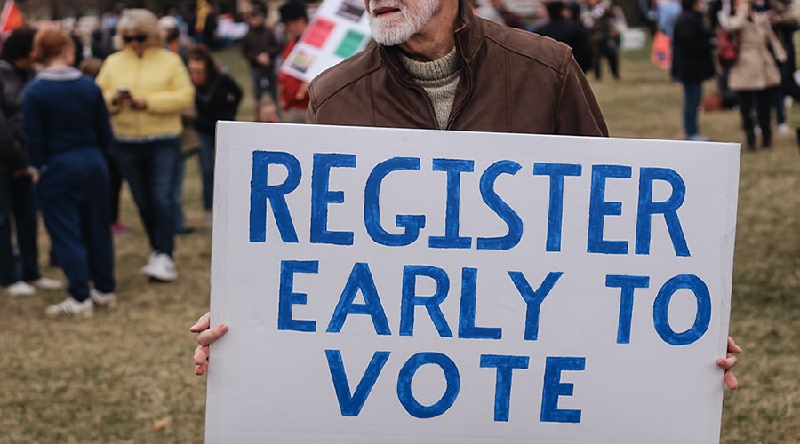 Man holding sign which says register early to vote