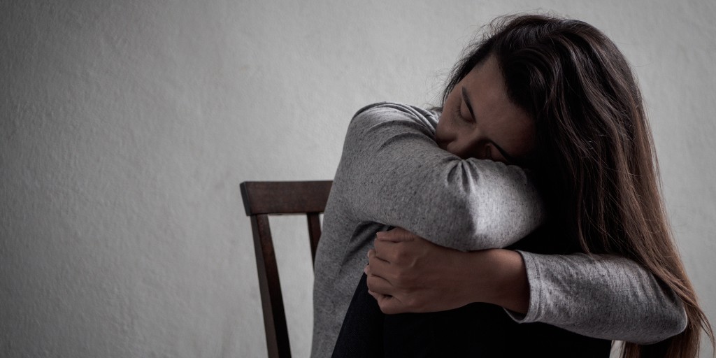 Sad woman with long brown hair sat with her head on her arms. Credit: Getty/spukkato