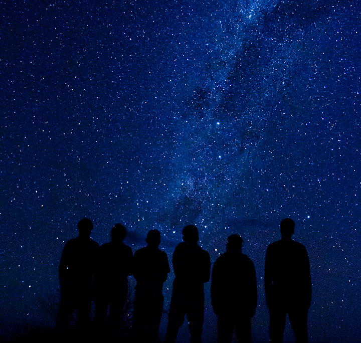 silhouette of six students in front of a starry night sky