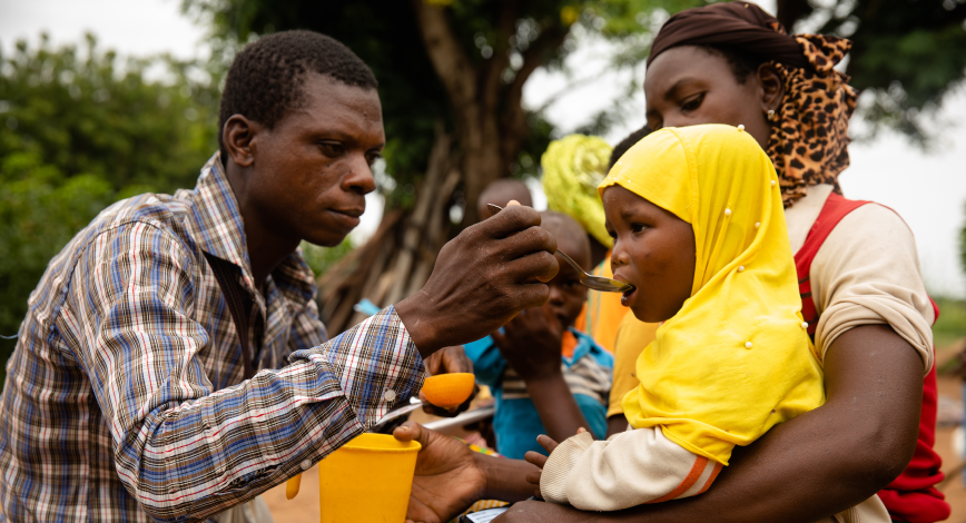 Man feeding a child which a woman is holding