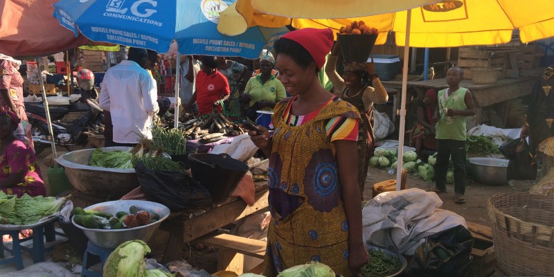 A young woman uses her phone at the market, Ghana, 2015.