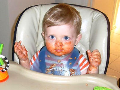 Baby boy having a messy meal in his high chair