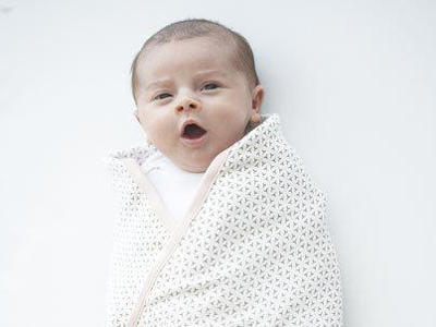 swaddled baby yawning on a white sheet