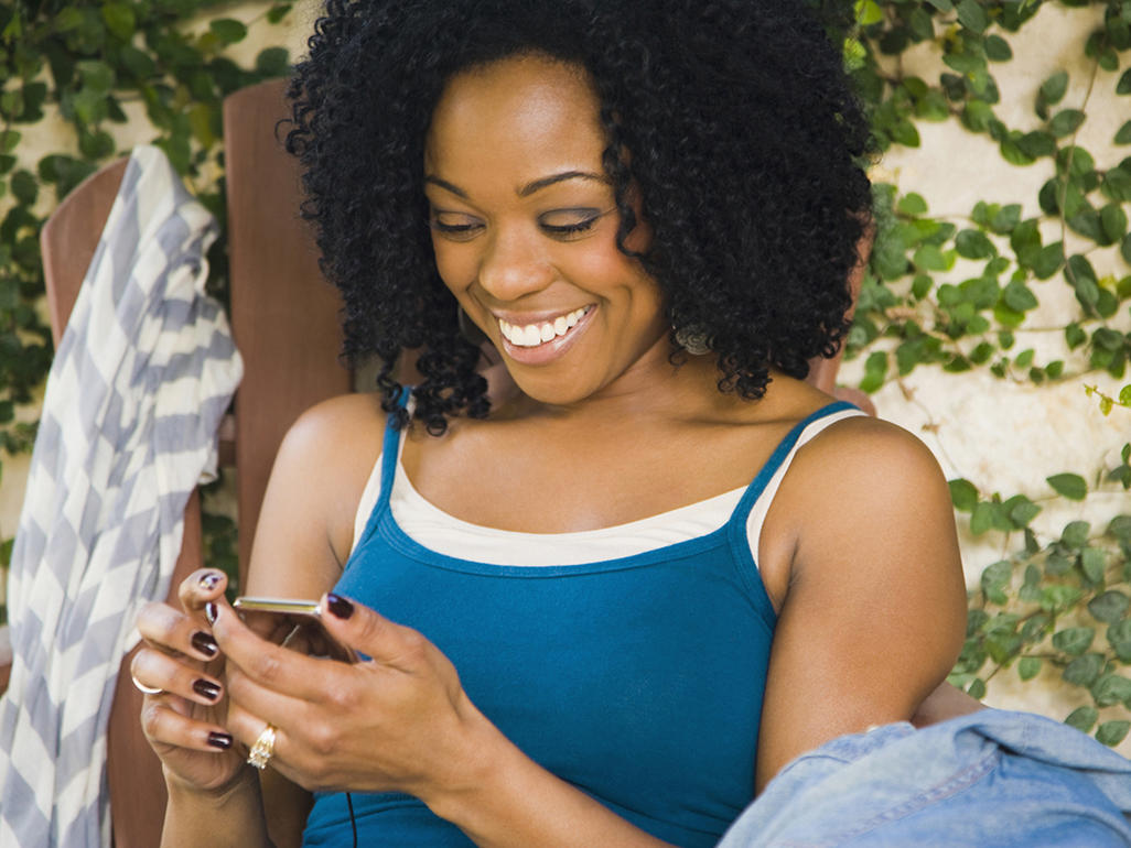 woman laughing while watching her mobile phone, sitting down on a chair