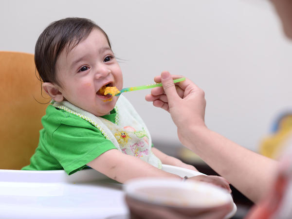 Mum feeding baby in a highchair first solid foods with a spoon