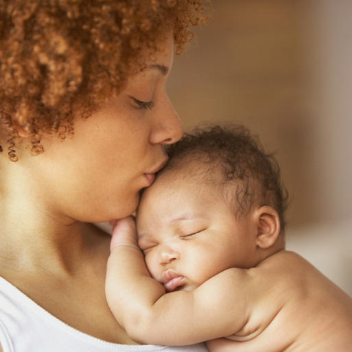 mother holding and kissing the forehead of sleeping baby