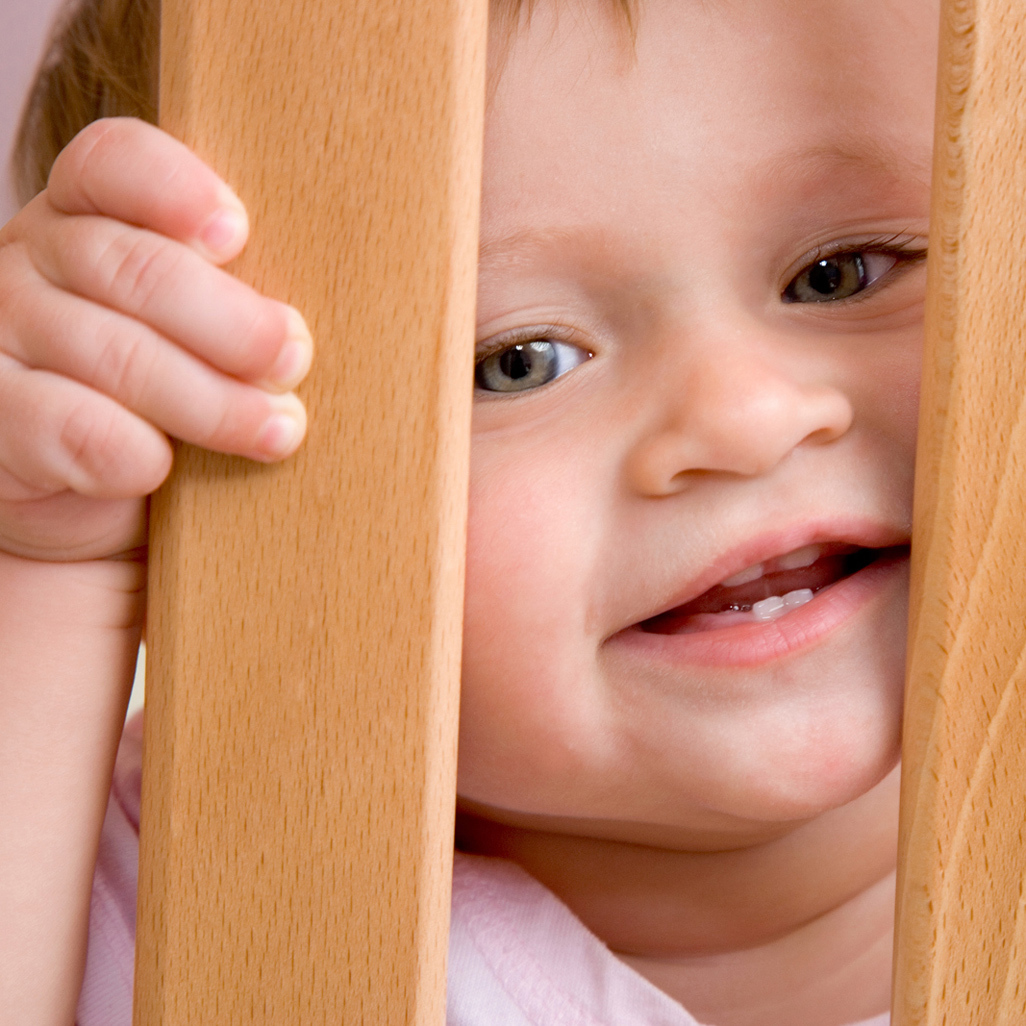 baby looking through wooden crib