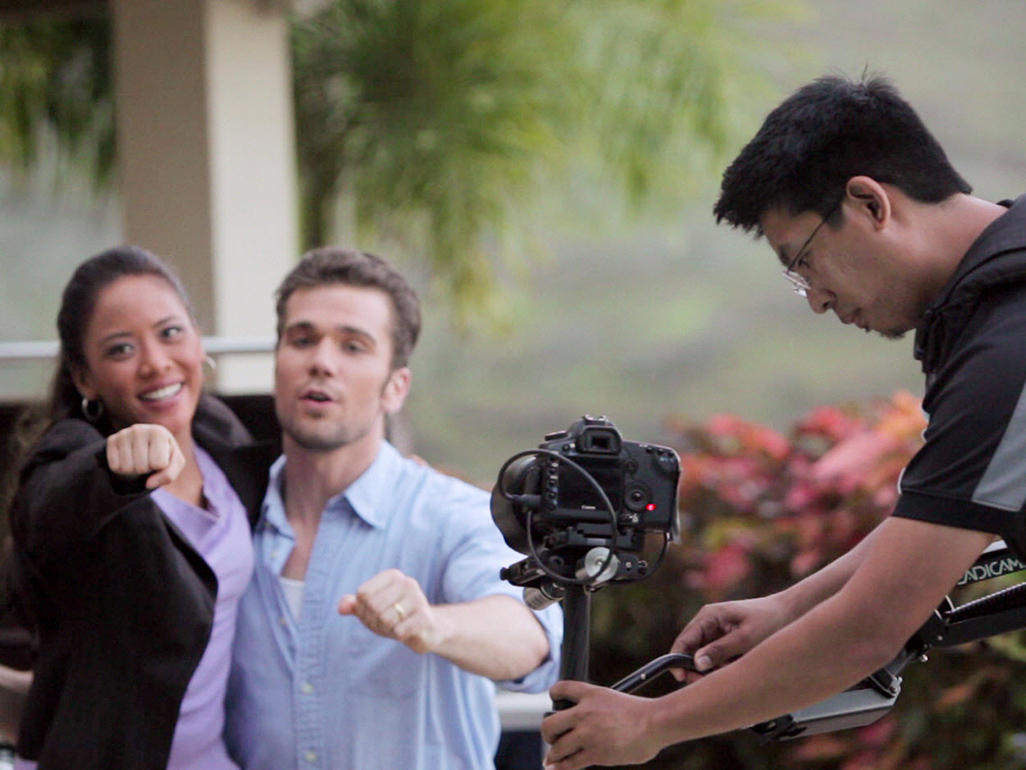 videographer adjusting camera in front of man and woman actors