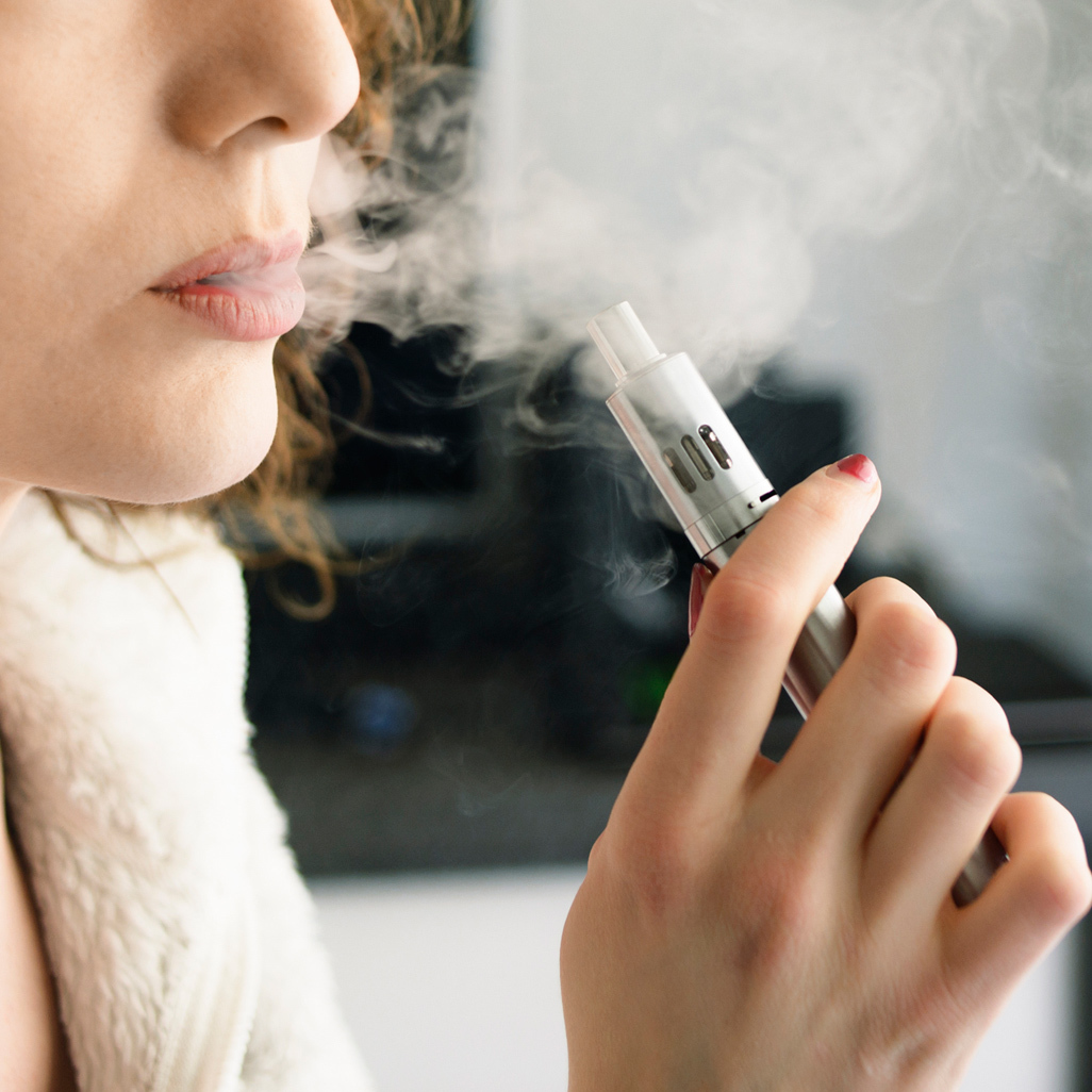 woman holding vape pen exhaling smoke