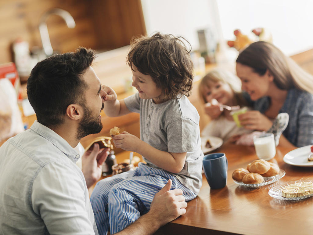 family eating while little boy is sitting on a table and holding his father's nose