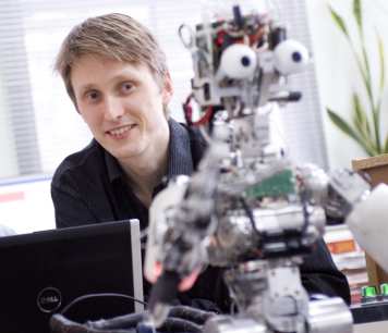 A man sitting behind a robot with googly eyes