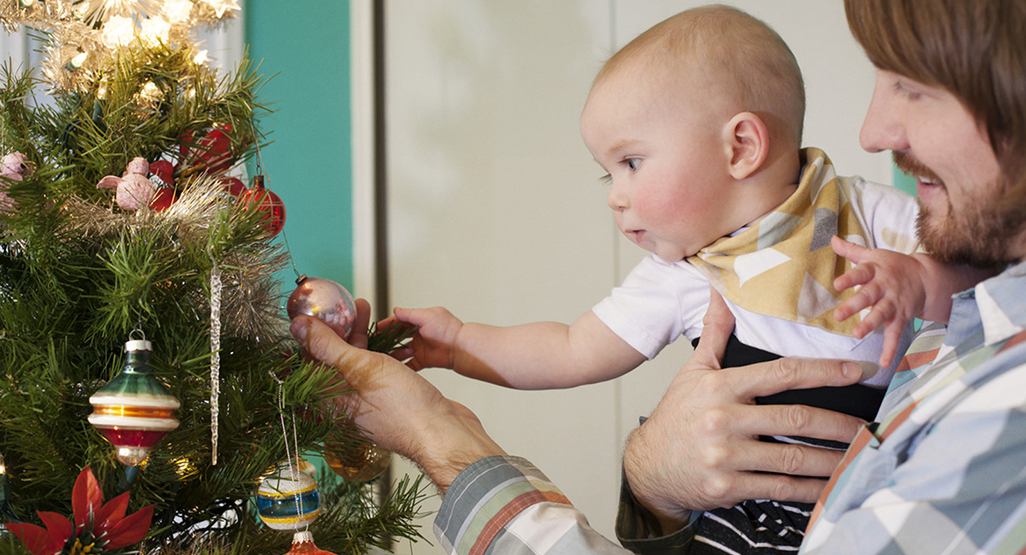 Papa und Baby schauen sich eine Weihnachtskugel am Baum an