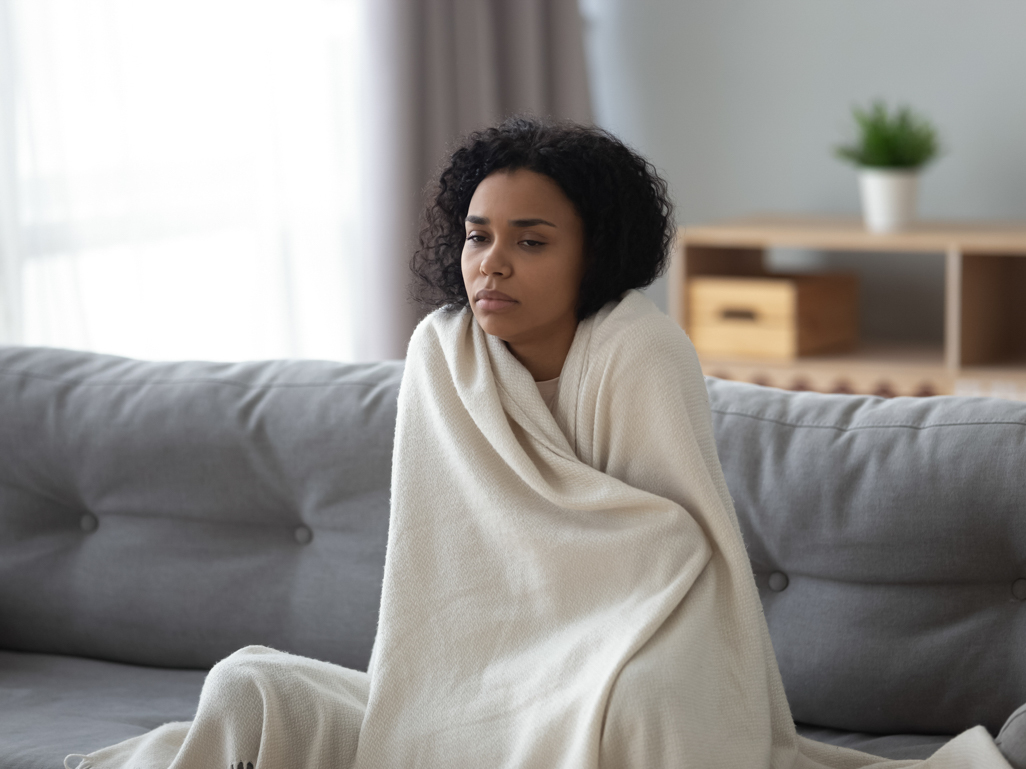 Pregnant woman on the sofa, hugging herself in blanket and looking concerned